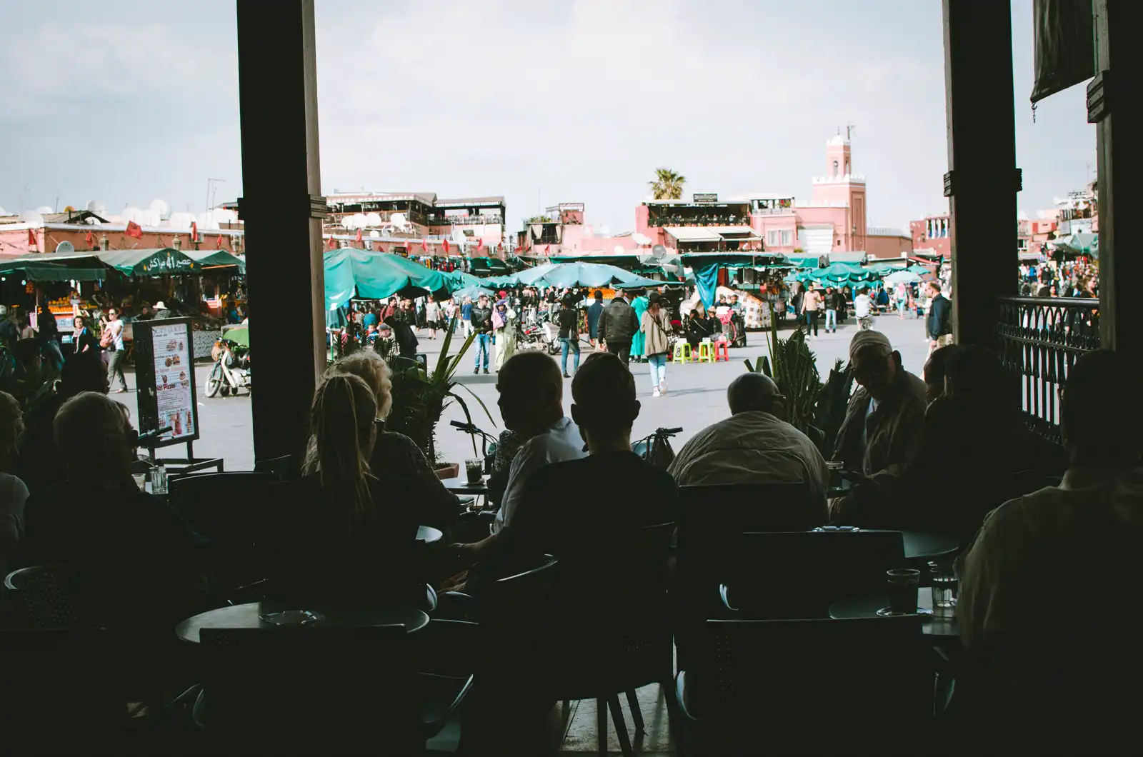 View from a shaded café over the bustling Jemaa el-Fnaa square and market stalls in Marrakech, Morocco