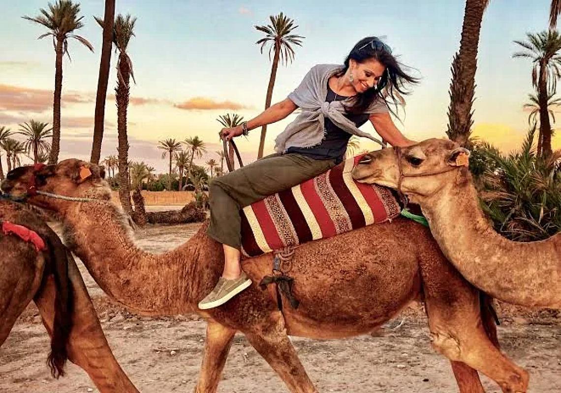 Traveller climbing onto a camel among Palmeraie palm trees