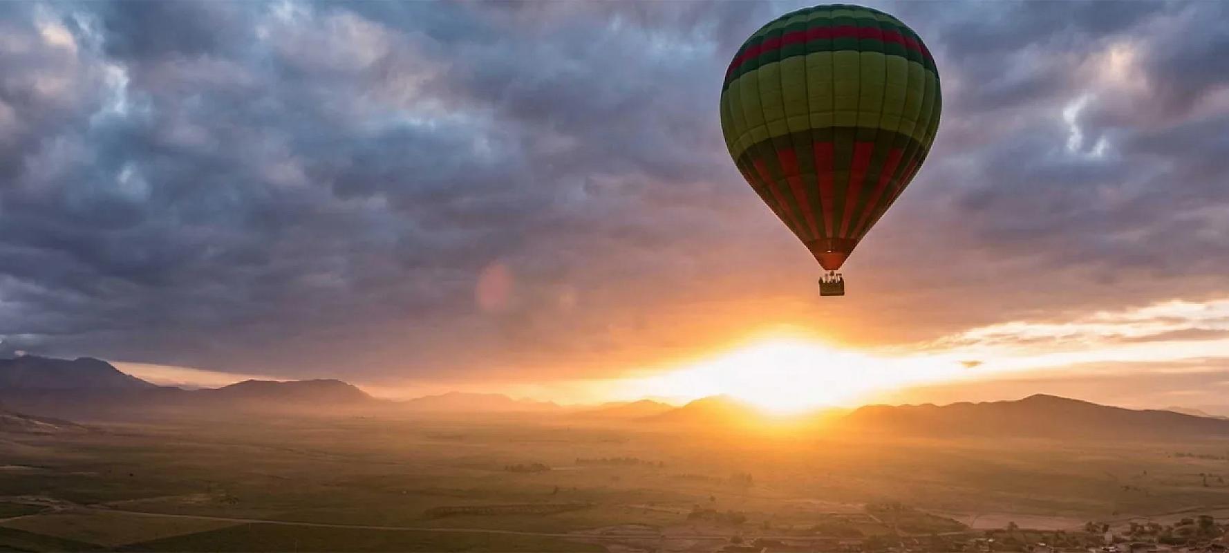 Hot air balloon drifting over plains towards the Atlas at sunrise