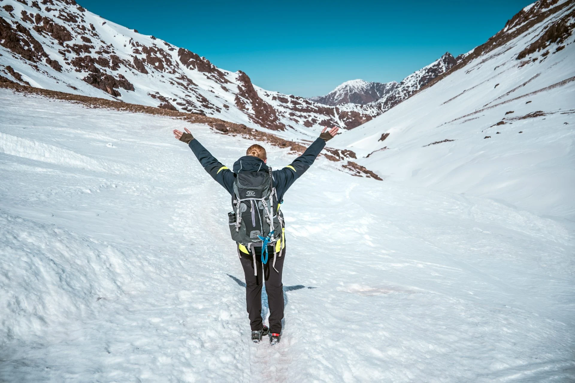 Trekker with raised arms in a snow-filled valley below Toubkal