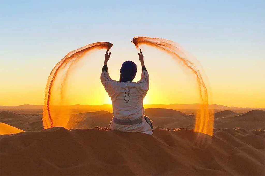 Guide throwing arcs of sand from a Merzouga dune at sunset