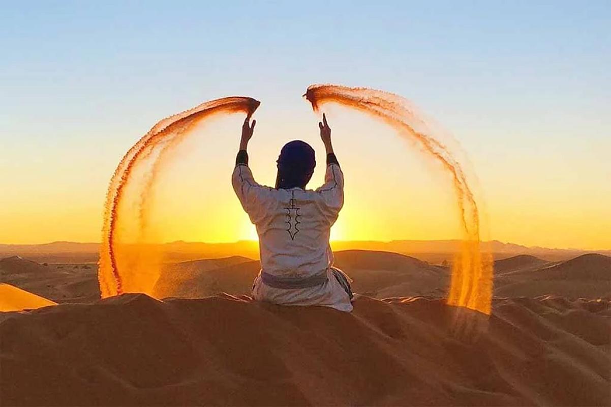 Guide throwing arcs of sand from a Merzouga dune at sunset
