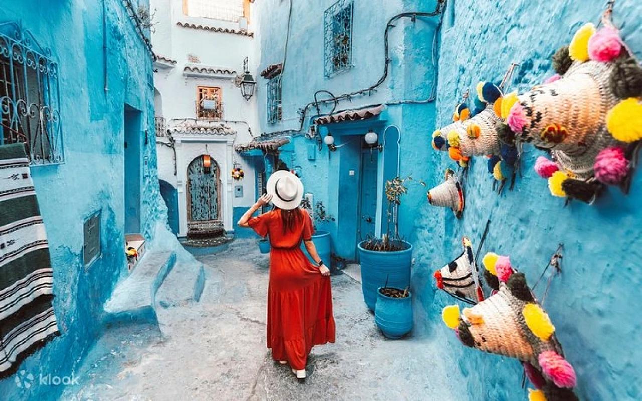 Woman in a red dress walking a bright blue Chefchaouen lane