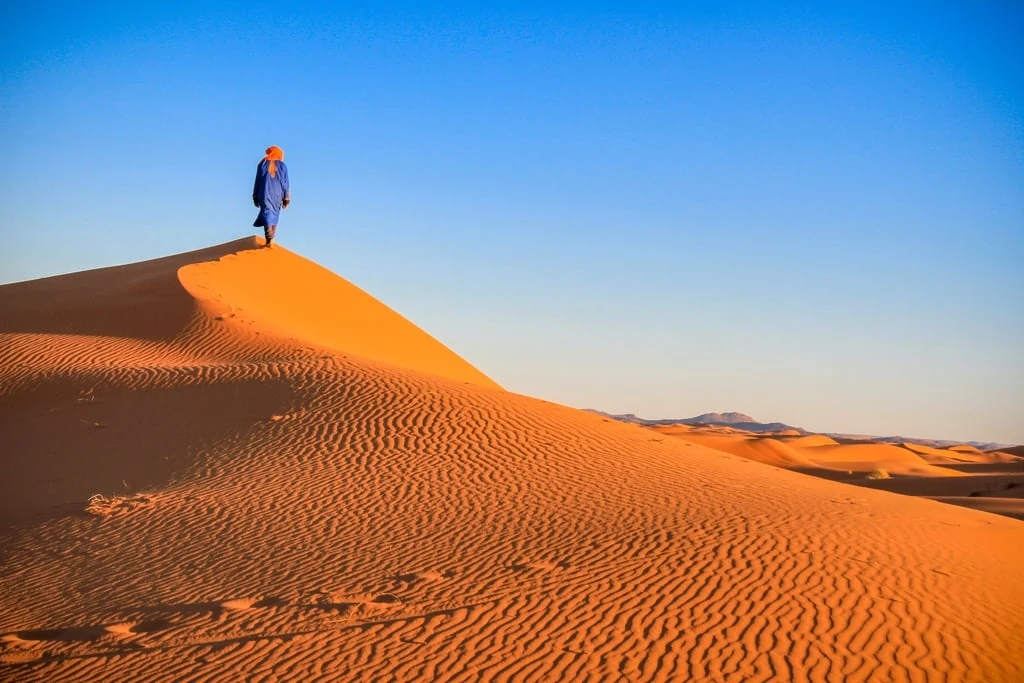 Blue-robed guide standing on a rippled Erg Chebbi dune