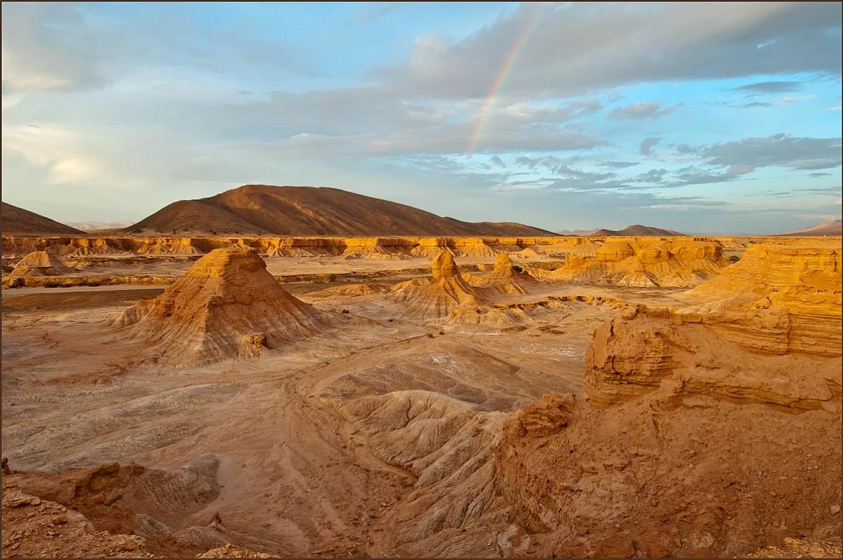 Eroded rock formations under a rainbow in the Zagora desert