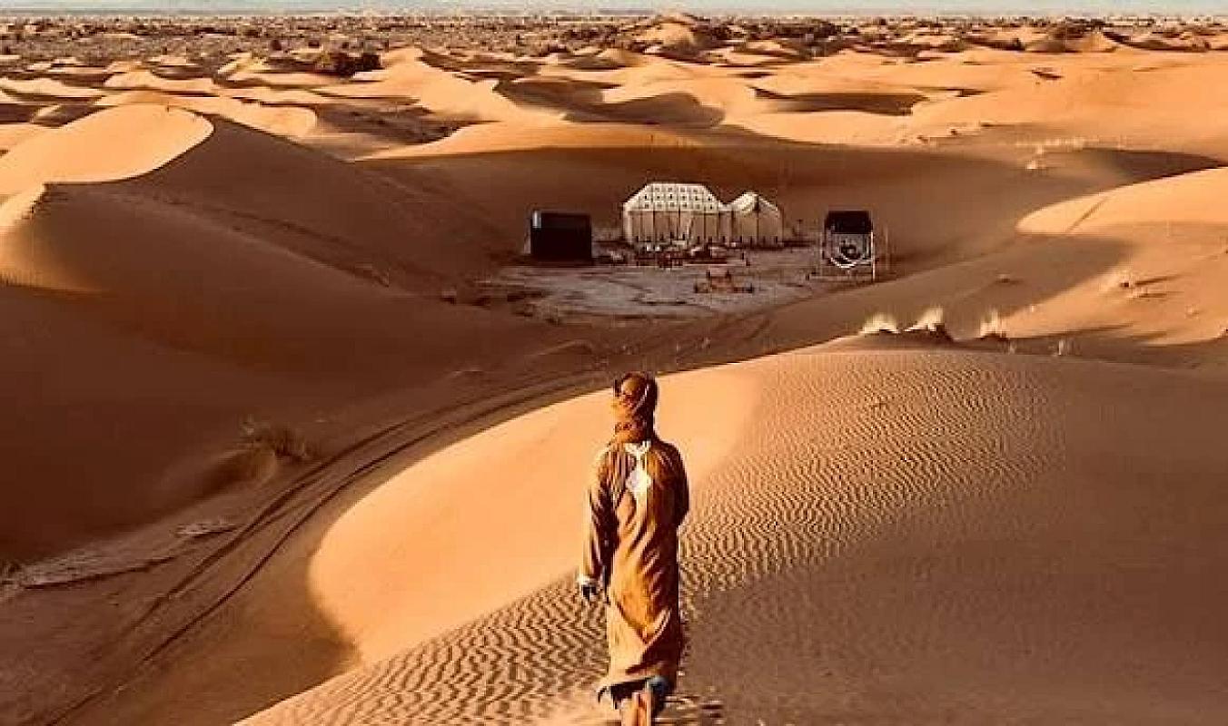 Traveller walking the Erg Chigaga dunes towards a desert camp