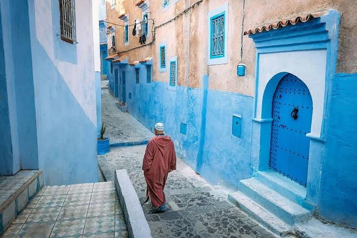 Man in a djellaba walking a blue alley of the Chefchaouen medina
