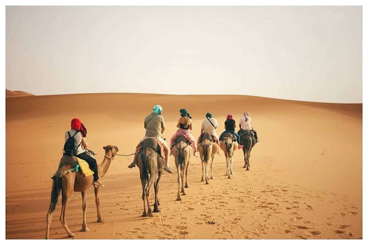 Group riding camels in line across the pale Merzouga dunes